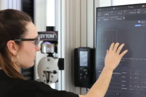 Ingeniera documentando resultados obtenidos por máquina de ensayo de tensión.