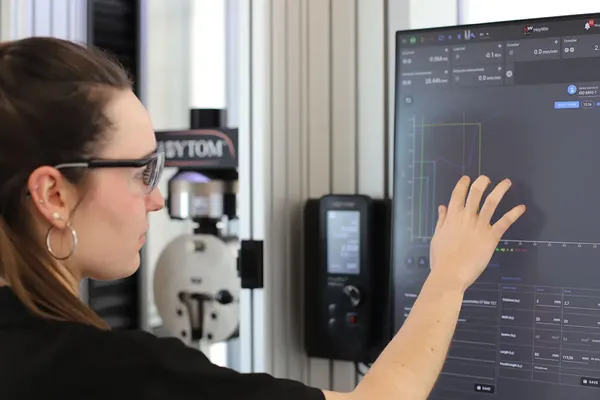Ingeniera documentando resultados obtenidos por máquina de ensayo de tensión.