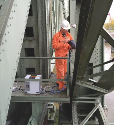 Técnico aplicando espectrometría sobre una estructura metálica de puente para analizar la composición de materiales en exteriores