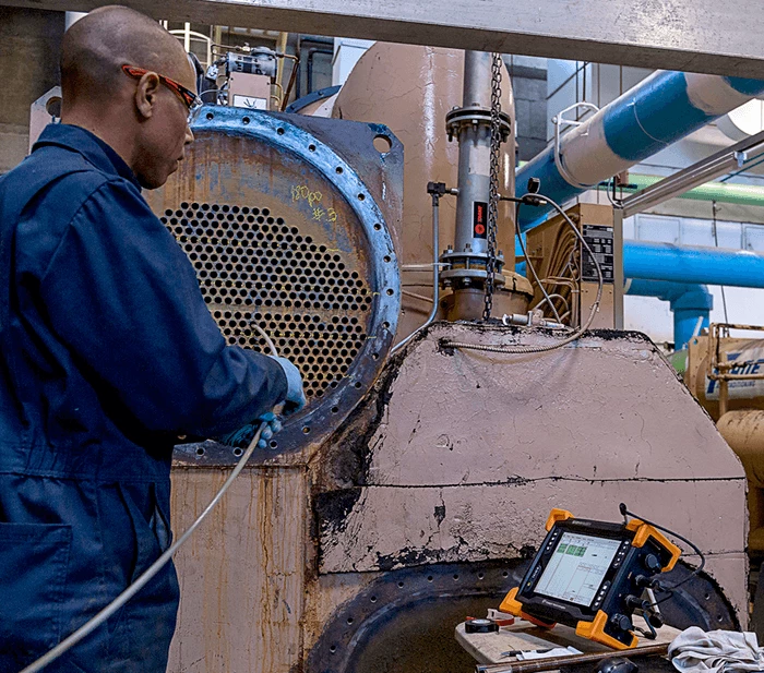 Cuáles son las pruebas no destructivas: Imagen de un técnico inspeccionando los tubos de un intercambiador de calor industrial, utilizando equipos de ensayos no destructivos.