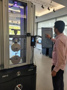 Un técnico especializado supervisa cuidadosamente el progreso de un ensayo de tensión en una pieza metálica en un laboratorio de materiales.