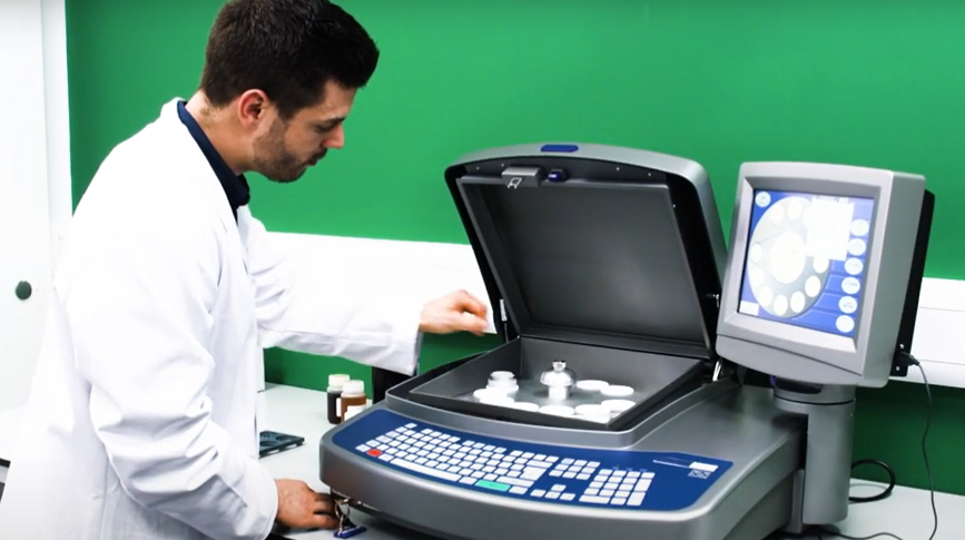 Un científico en un laboratorio realiza el análisis de fluorescencia de rayos X utilizando un equipo de sobremesa con muestras en viales.
