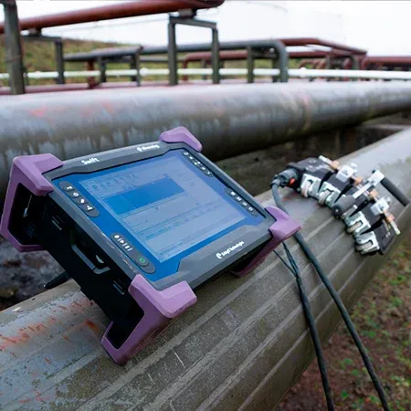 Una tableta resistente Swift está configurada sobre un oleoducto de gran diámetro, mostrando una interfaz de software con gráficos y datos de MFL para detectar corrosión.