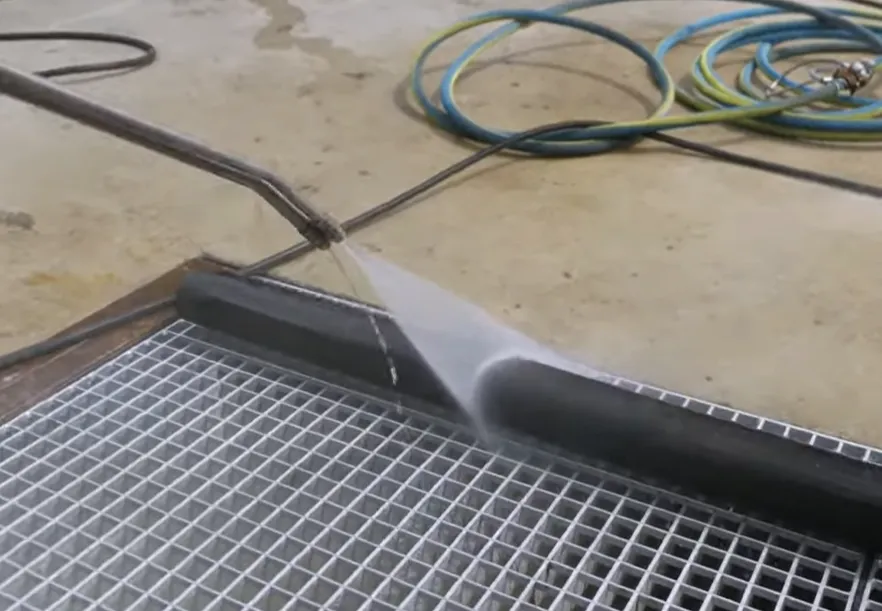 Chorro de agua a presión limpiando una superficie sobre una rejilla metálica, paso esencial antes de aplicar la protección anticorrosiva para garantizar la adherencia del recubrimiento.