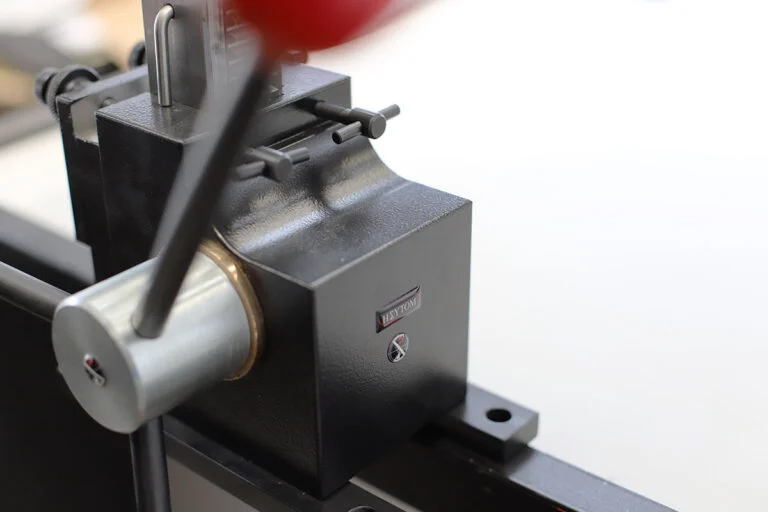 Brochadora manual con su caja de mecanismos y un brazo de palanca en movimiento, creando un efecto de desenfoque dinámico