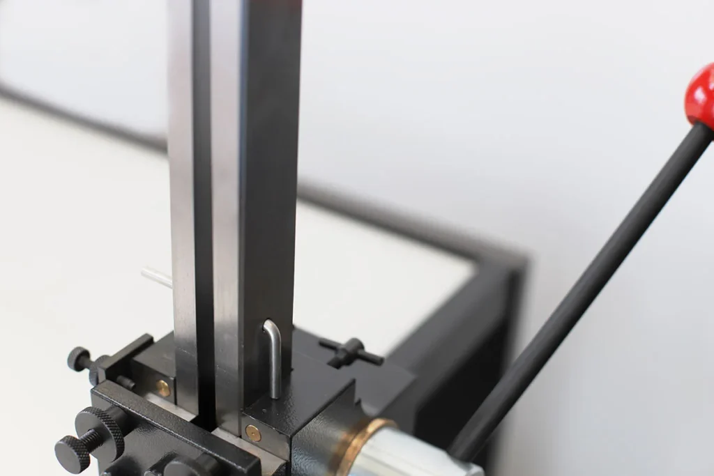 Primer plano de la sección superior de una brochadora manual, mostrando la guía vertical y el pin metálico de sujeción