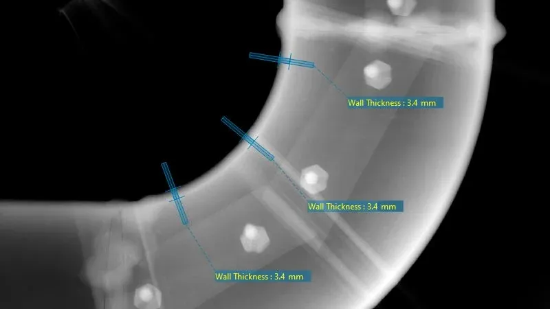 Radiografía industrial mostrando mediciones precisas del espesor de pared en una sección curva de tubería para control de calidad