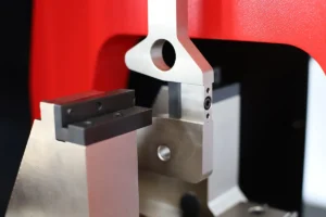 Primer plano del filo del martillo y el soporte de la muestra en un equipo de ensayo de impacto, conocido como péndulo Charpy.