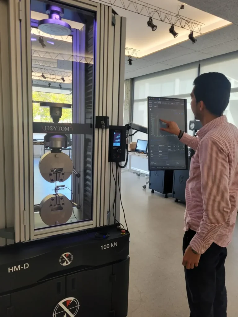 Técnico examinando los resultados en la pantalla de una máquina universal de ensayo de tensión que realiza una prueba de tracción en un material