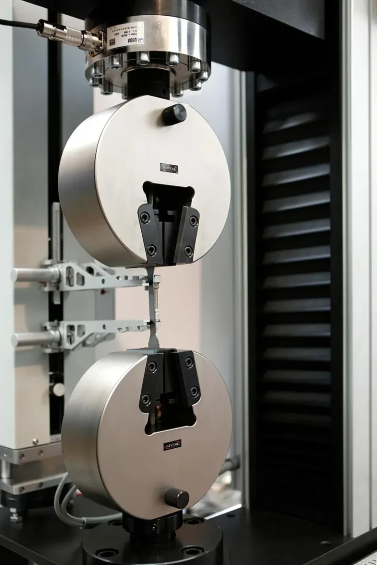 Detalle del sistema de sujeción de una máquina de ensayo de tensión, mostrando las mordazas que sostienen una pequeña probeta de material