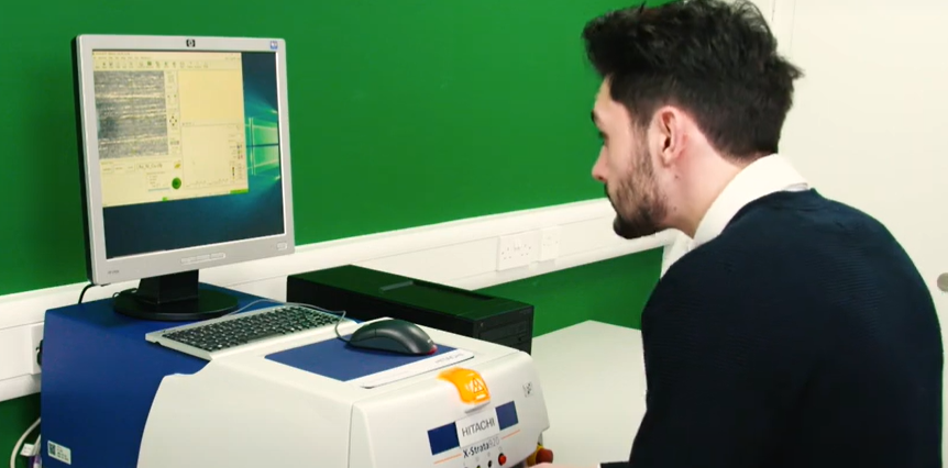 Un científico o técnico opera un analizador de fluorescencia de rayos X (XRF) de banco conectado a una computadora para procesar resultados.