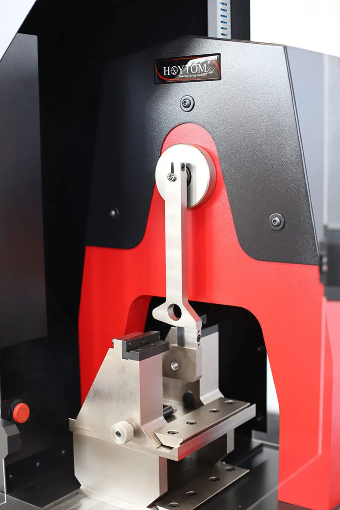 Vista media de un equipo de ensayo de impacto Hoytom, mostrando el péndulo Charpy en su mecanismo de liberación.