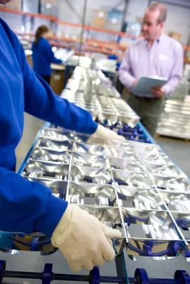 Personal de planta verificando la integridad de componentes reflectantes terminados sobre una cinta transportadora azul.