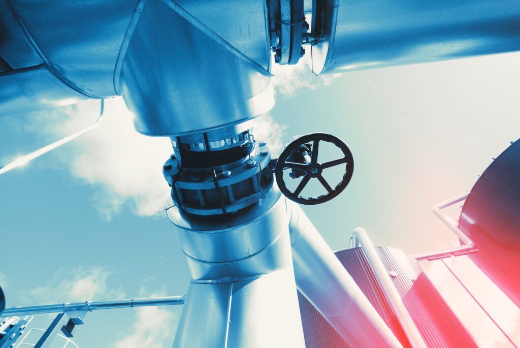 Primer plano de conexiones metálicas y una gran válvula de rueda en una planta de la industria del petróleo y gas.