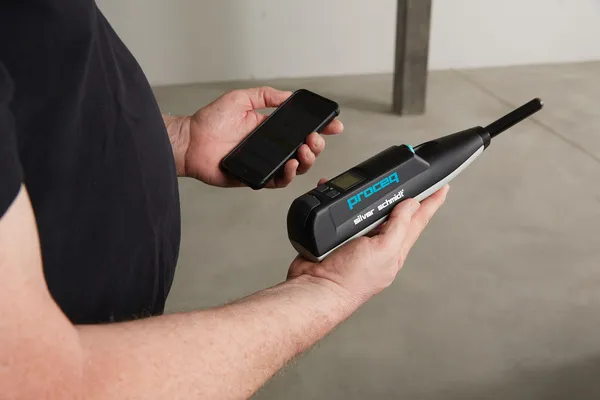 Operador sosteniendo un esclerómetro inteligente y un celular para la gestión de mediciones mediante una aplicación