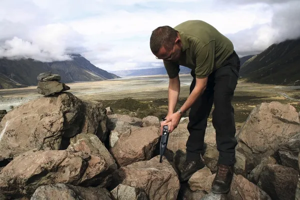 Técnico realizando pruebas de campo con un esclerómetro sobre formaciones rocosas naturales en un paisaje montañoso