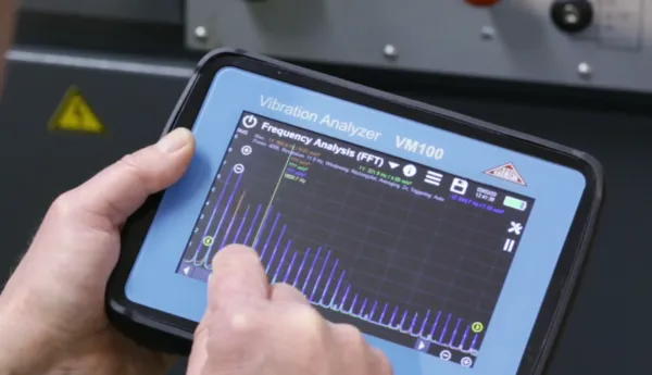 Un técnico de mantenimiento de equipo toca la pantalla de un analizador de vibraciones VM100 para evaluar los datos de una máquina industrial.