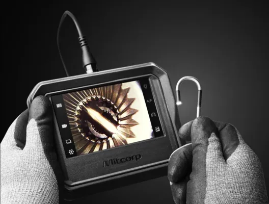 Especialista con guantes de seguridad operando una sonda de videoscopia para iluminar y revisar un piñón de acero fino.