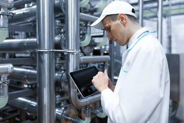 Especialista con bata blanca usa una tableta para el control de procesos industriales en un sistema de tuberías.