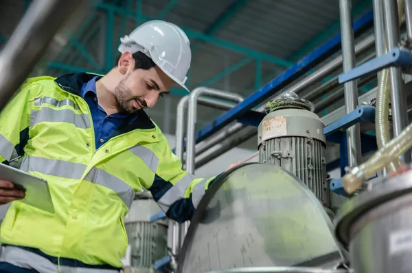 Ingeniero sonriente con casco inspecciona un motor eléctrico durante el control de procesos industriales en planta.