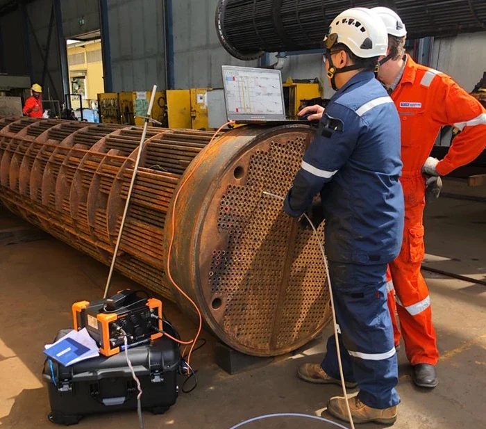 Expertos de empresas de ensayos no destructivos en Perú inspeccionan tubos de un intercambiador de calor industrial.