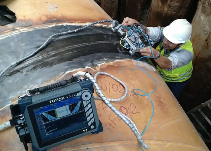 Especialista calibra un escáner automatizado de phased array sobre la soldadura curva de un gran tanque de acero.