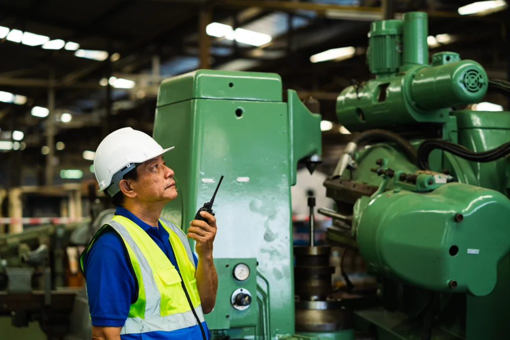 Supervisor de fábrica usando radio cerca de maquinaria pesada bajo estrategias de integridad industrial.