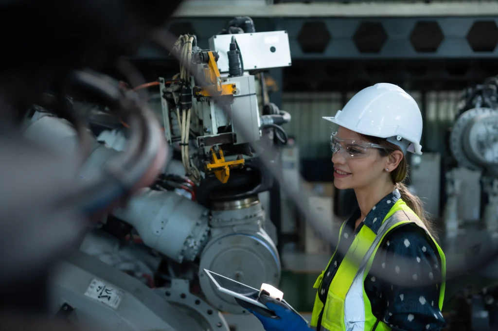 Ingeniera sonriente con tableta inspeccionando maquinaria bajo estrategias de integridad industrial.