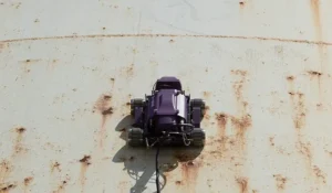 Robot oruga trepador realizando inspección automática con equipo de medición por ultrasonido industrial en tanque corroído.