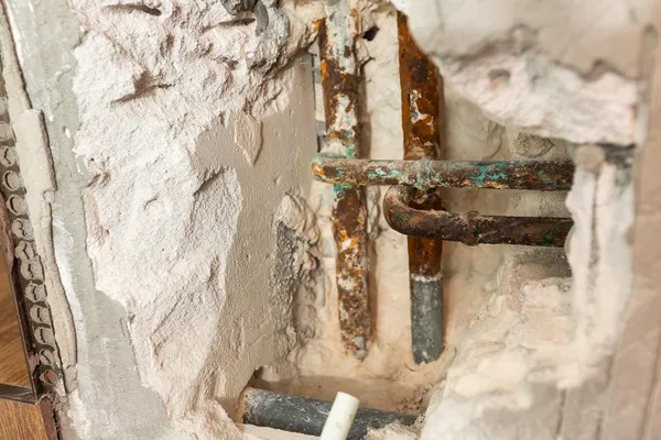 Vista cercana de tuberías deterioradas con corrosión por picaduras expuestas en el interior de un muro.