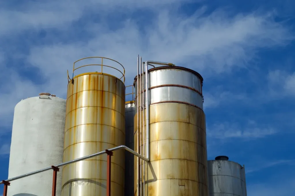 Inspección de fondos de tanques industriales: Tanques de metal con signos de corrosión y tuberías, bajo cielo con nubes.