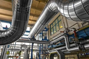 Fotografía que muestra grandes tuberías plateadas y otras más pequeñas con válvulas en un entorno industrial, esencial para la integridad de tuberías. Fotografía que muestra grandes tuberías plateadas y otras más pequeñas con válvulas en un entorno industrial, esencial para la integridad de tuberías.