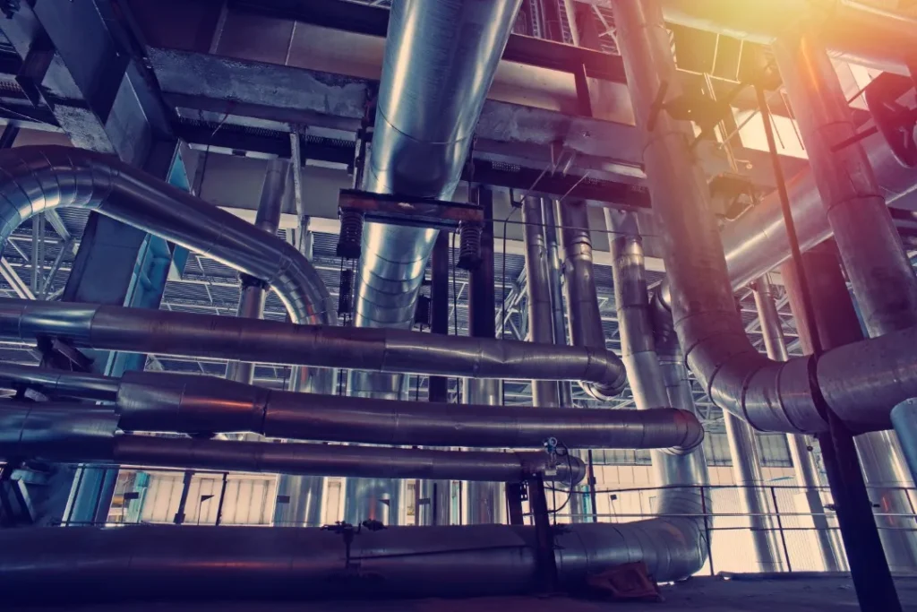 Primer plano de una sección de tuberías industriales gruesas y plateadas con luz solar intensa, fundamental para la integridad de tuberías.