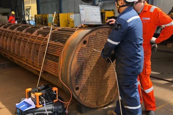 Expertos de empresas de ensayos no destructivos en Perú inspeccionan tubos de un intercambiador de calor industrial.